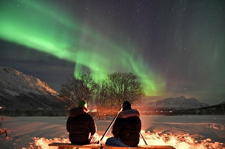 Du khách mặc áo ấm đứng ngắm cực quang giữa tuyết trắng Lapland