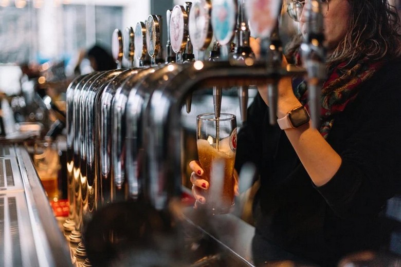 Hàng tay kéo bia cask ale bằng sứ trên quầy pub với ly pint vàng óng đặt cạnh