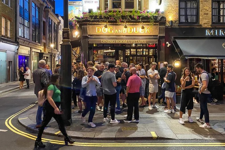 Mặt tiền một pub cổ ở Anh với biển hiệu gỗ sơn hình vương miện và giỏ hoa treo