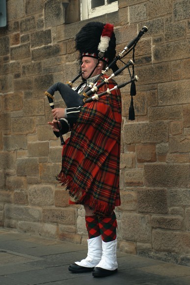 Người đàn ông Scotland mặc kilt kẻ tartan đỏ thổi kèn bagpipe trước lâu đài Edinburgh