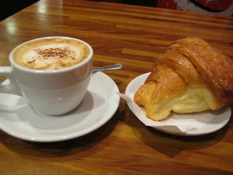 Tách cappuccino với bọt sữa dùng vào buổi sáng cùng bánh cornetto